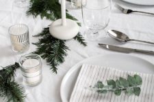 22 a minimalist table setting with an evergreen garland, white candles and eucalyptus for marking each place setting