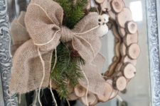 22 a wood slice Christmas wreath with evergreens, pinecones and a large burlap bow on the side