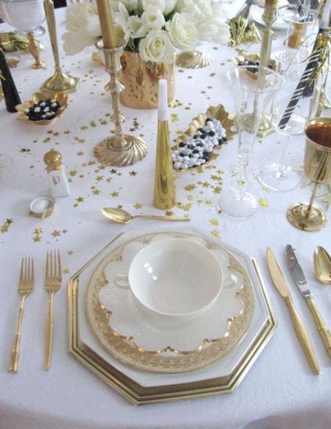 a white and gold tablescape with gold cutlery, goblets, candle holders and white blooms