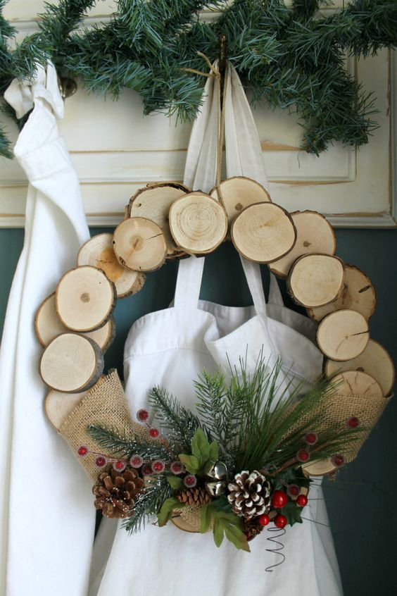 a wood slice Christmas wreath with faux evergreens, bells, berries and snowy pinecones for a rustic feel