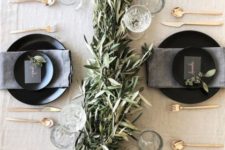 26 a neutral tablescape with a greenery garland, glasses, matte black plates and chargers and gold cutlery
