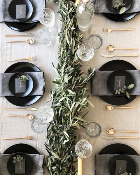 a neutral tablescape with a greenery garland, glasses, matte black plates and chargers and gold cutlery