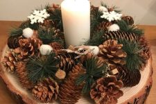 a Christmas arrangement of a tree slice, pinecones, evergreens, snowflakes and a pillar candle