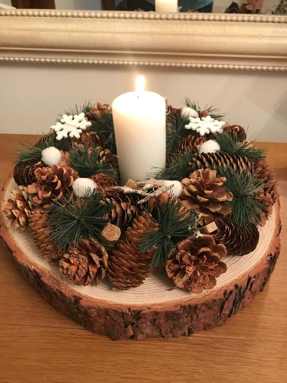 a Christmas arrangement of a tree slice, pinecones, evergreens, snowflakes and a pillar candle