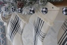 a Christmas mantel with plaid stockings, a buffalo check bead garland, an evergreen and bead one, pinecones and berries