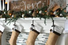 a beautiful rustic Christmas mantel styled with tine balls, silver ornaments, pinecones, evergreens, burlap stockings and a crate with firewood