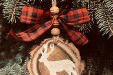 a beautiful rustic Christmas ornament made of a wood slice with a live edge, wooden beads and a plaid bow