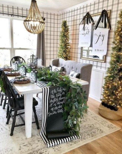 a chic farmhouse Christmas dining room with tall Christmas trees, a greenery runner, a striped and chalkboard runner, signs and candles