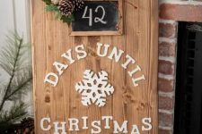 a cute Christmas sign of a wooden plaque with white letters, a red turck, evergreens, pinecones and a chalkboard house number