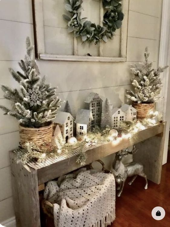 a farmhouse Christmas console table with flocked Christmas trees, houses, evergreens and ornaments and a deer under the table