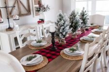 a farmhouse Christmas dining room with a cotton wreath, snowy Christmas trees, a plaid runner, candles and woven placemats