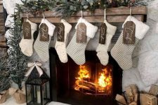 a farmhouse Christmas mantel with evergreens, pinecones, stockings, wooden tags and a candle lantern