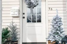 a farmhouse Christmas porch with snowy Christmas trees, candle lanterns, a snowy Christmas wreath is a very cozy space