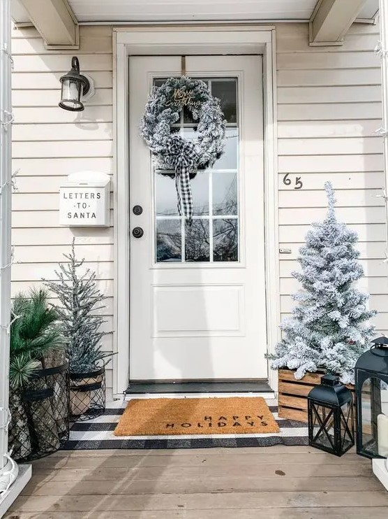a farmhouse Christmas porch with snowy Christmas trees, candle lanterns, a snowy Christmas wreath is a very cozy space