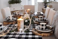 a farmhouse buffalo check Christmas tablescape with plaid linens, wood slice placemats, antlers and moss and candles wrapped with bark