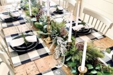 a natural Christmas table setting with buffalo check placemats, black plates, an evergreen garland with pinecones and candles