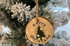 a rustic Christmas ornament of a tree slice with a black tree and snow is a lovely idea that can be easily realized