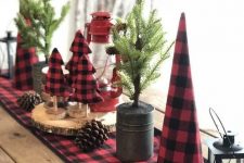 a rustic Christmas tablescape with a red plaid runner and matching fabric trees, potted Christmas trees with pinecones and wood slices