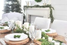 a rustic Christmas tablescape with an uncovered table, a greenery runner with candles, wood slice placemats