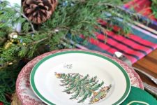 a traditional Christmas table with wooden slice chargers, printed plates, evergreens and pinecones plus candles and green napkins