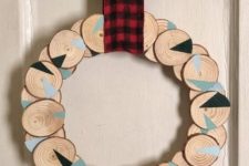 a wood slice Christmas wreath with geometric design and a plaid ribbon is a cool bold decoration idea