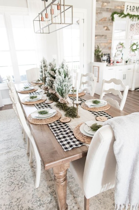an airy farmhouse Christmas table with a burlap runner, woven chargers, wood slices with monograms, flocked mini trees and candkes
