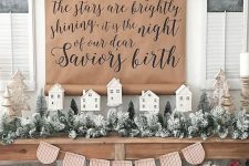 farmhouse Christmas decor with flocked evergreens, a sign, houses and a bunting, berries and cotton