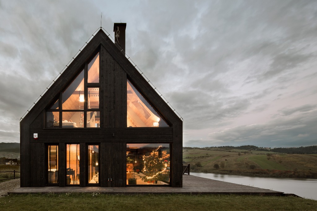 This black lakeside cottage features a gabled roof, a deck and lots of windows to enjoy the views