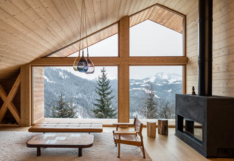 This is the living room of the chalet with a large sloped window, a large hearth and a selection of modern furniture