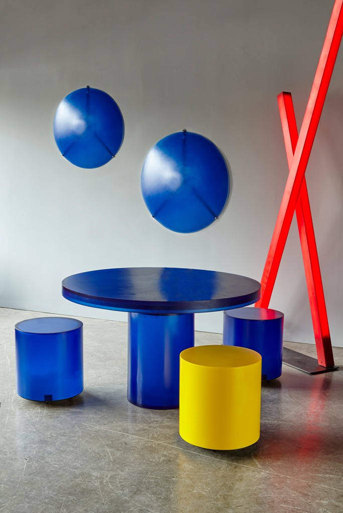 The round Chief stool has a cylindrical form, in blue, yellow or red, and the table has a circular surface and a single leg and is made from blue resin