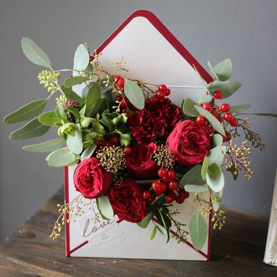 a stylish centerpiece of a burgundy lined envelope filled with bold blooms and greenery