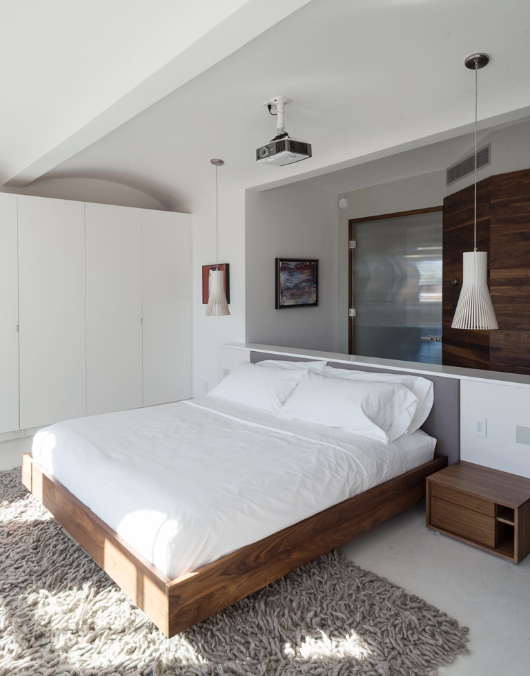 One of the bedrooms with a floating bed, pendant lamps and a wardrobe with natural wood touches