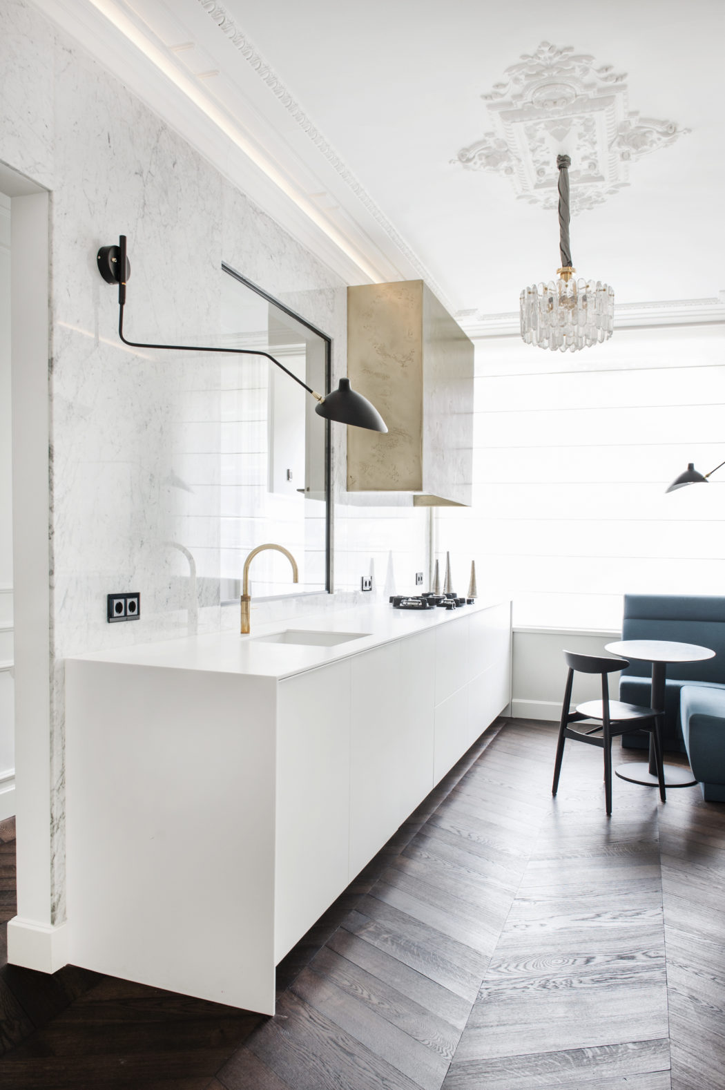 The kitchen is done with a marble backsplash, a white cabinet, a hanging metallic one and a bold glam chandelier