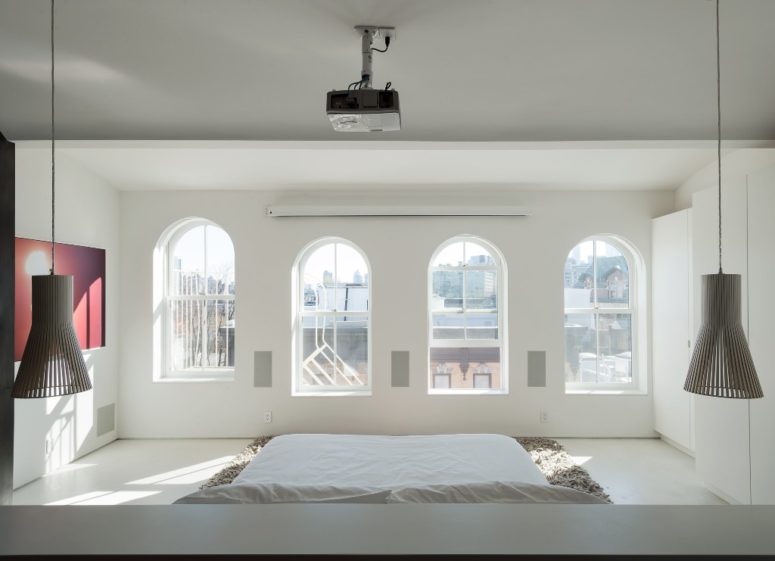 The master bedroom shows lots of windows that bring much light in and a bed placed on the floor