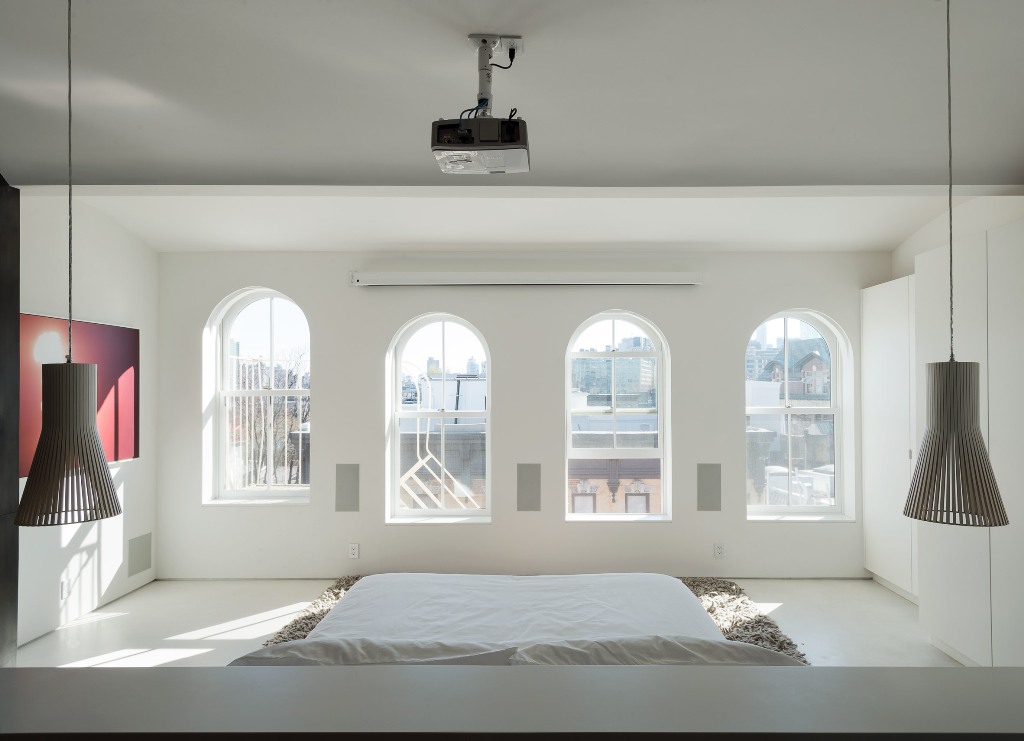 The master bedroom shows lots of windows that bring much light in and a bed placed on the floor