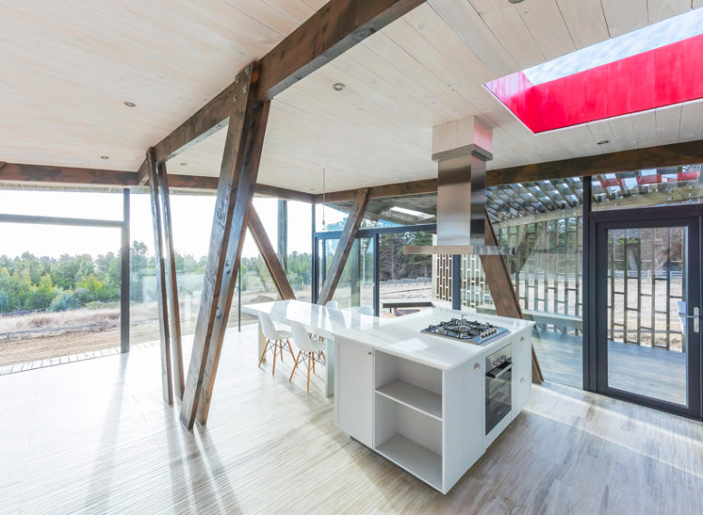 The kitchen is done with minimalist white furniture and wooden beams that echo with the wooden shell outside