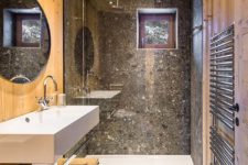 06 The master bathroom is clad with wood and stone-looking grey tiles, there’s a shower space