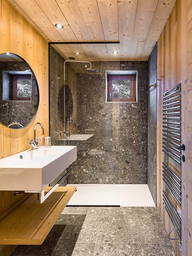The master bathroom is clad with wood and stone looking grey tiles, there's a shower space