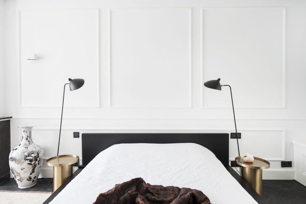 The master bedroom is done with white wainscot walls, black furniture and brass nightstands