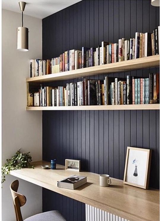 a black wall and light-colored wooden floating shelves plus a desk below for reading and studying