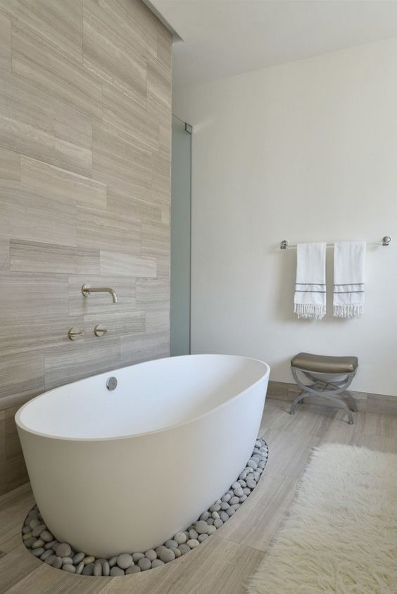 a wood clad wall and some pebbles under the bathtub add a spa feel to the space