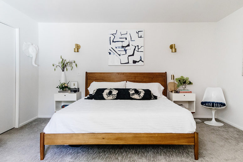 The bedroom features a wooden bed, white floating nightstands and some brass touches