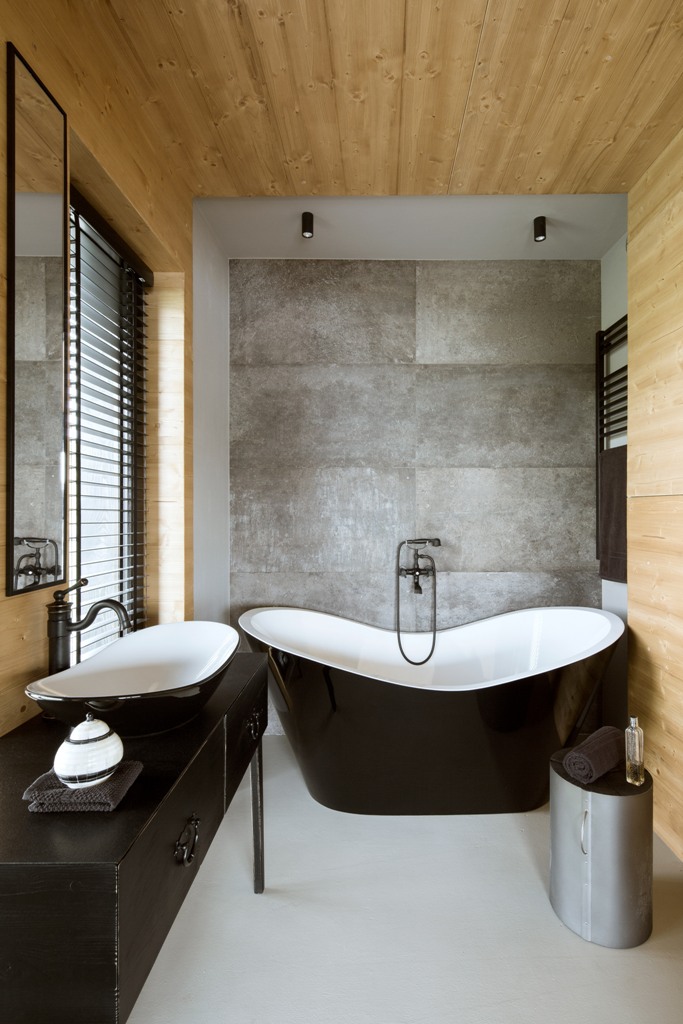 The master bathroom is clad with light-colored wood, there's a concrete wall and an elegant black sink and bathtub