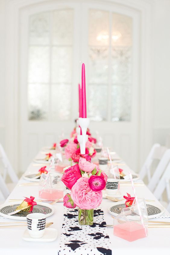 a black and white table setting with pink and hot pink florals and candles