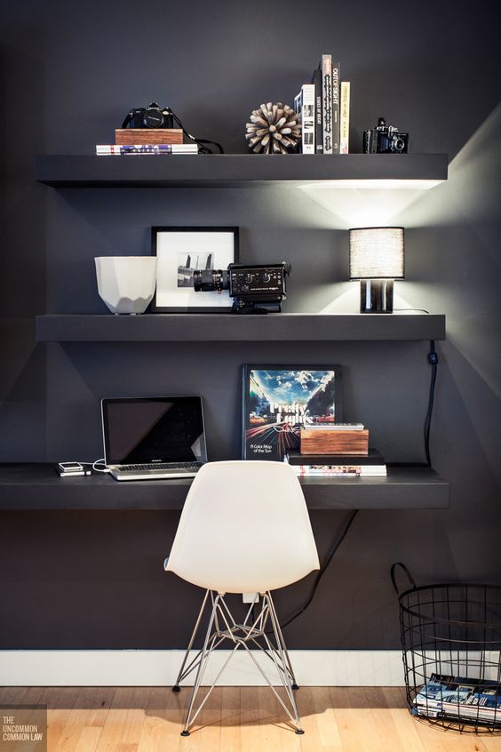 a black wall with floating shelves and a desk with displays and much light
