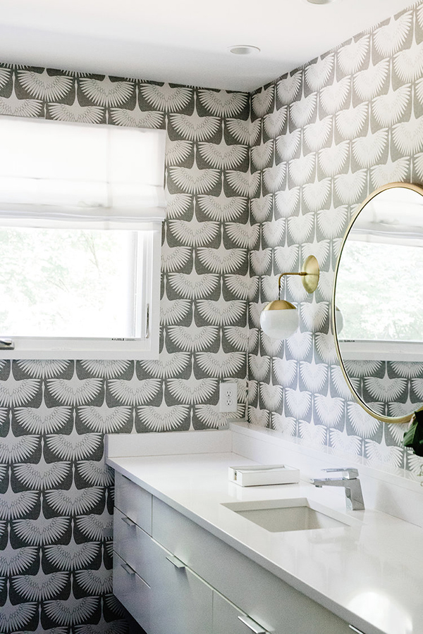 The bathroom is decorated with statement wallpaper and bold brass touches