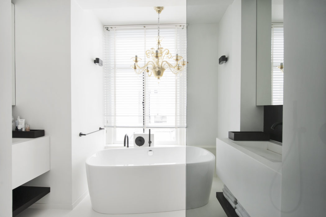 The master bathroom is done in white, with black accents and a brass chandelier over the bathtub