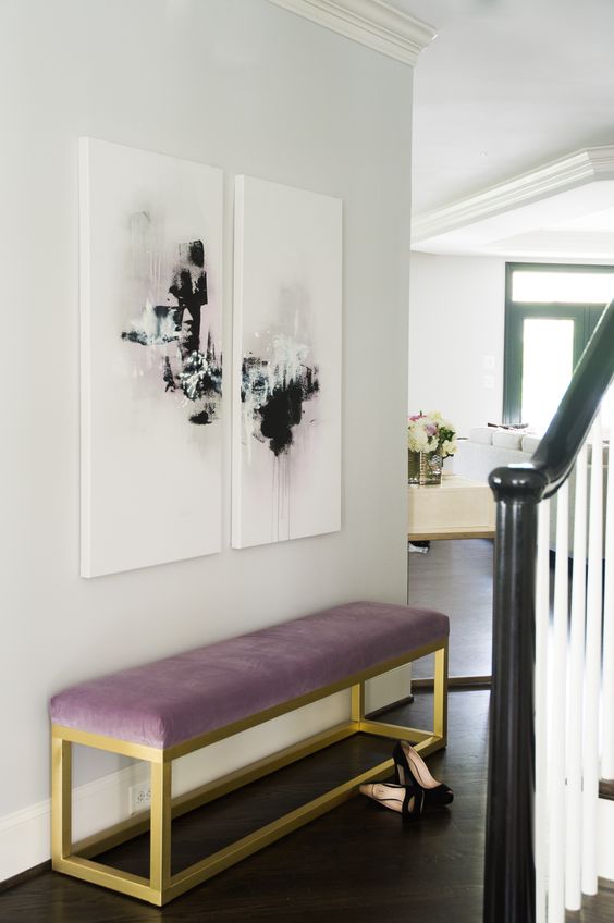 a modern glam entryway is nailed with a mauve upholstered bench and cool abstract artworks