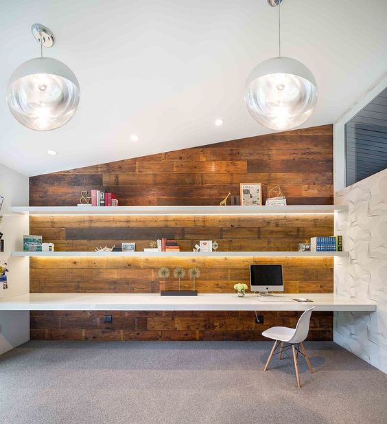 a modern home office with lit up floating shelves and a matching desk in fonrt of a reclaimed wood wall