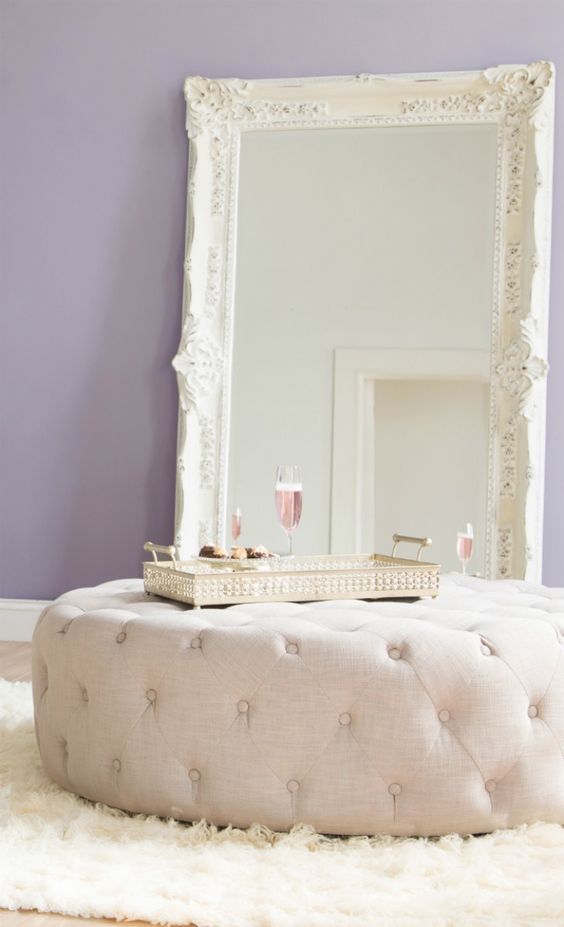 an oversized creamy ottoman plus a large vintage mirror add glam to the bedroom